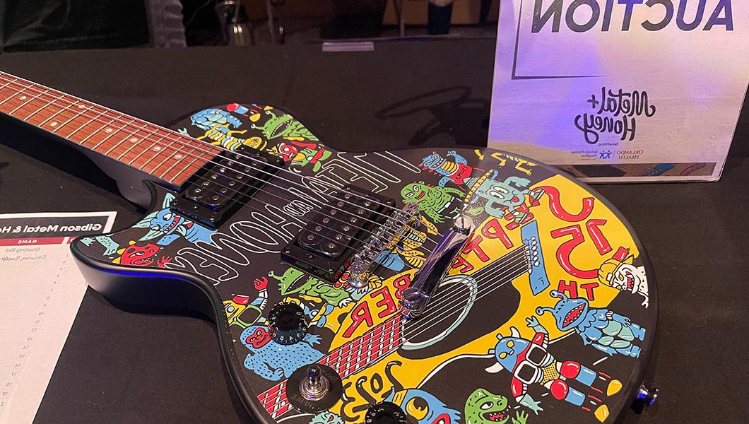 这是一把黑色电吉他的琴身，上面有彩色的图案贴花，旁边是一个写着“无声拍卖”的牌子.”